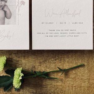 Op de afbeelding: Een witte kaart met de tekst "Hello Baby!" in cursief schrift. De kaart ligt naast een witte kaart met de tekst "Wren Allengford" in cursief schrift. De tekst "07.12.2021 | 02:19 | 6LBS 9OZ" is onder de naam gedrukt. De tekst "Bedankt voor al de liefde, wensen, kaarten en cadeaus. Ik ben een heel gelukkig klein baby" is onder de datum en tijd gedrukt.
