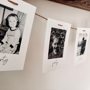 May include: A string of black and white photos of a young boy at different ages, each photo is labeled with the age of the boy. The photos are hung on a wall with twine.
