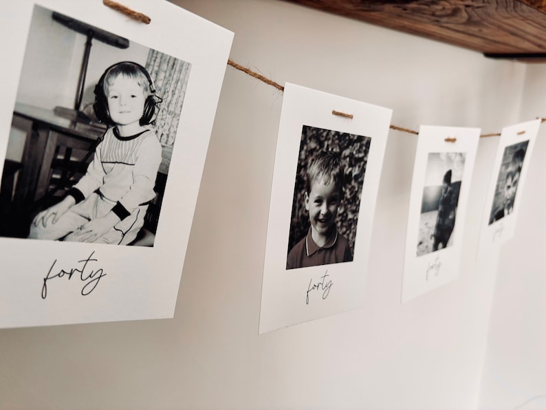 May include: A string of black and white photos of a young boy at different ages, each photo is labeled with the age of the boy. The photos are hung on a wall with twine.
