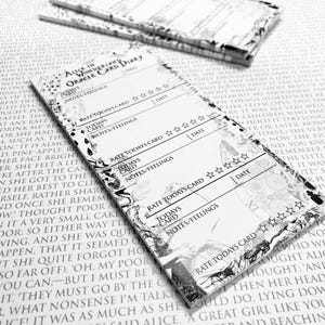 Könnte beinhalten: Schwarz-weißes "Alice im Wunderland" Orakelkarten-Tagebuch. Das Tagebuch bietet Platz, um die Tageskarte zu bewerten, Notizen und Gefühle festzuhalten und ein Datum einzutragen.