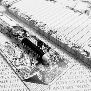 Op de afbeelding: Een zwart-wit notitieboekje met een fantasierijk Alice in Wonderland-ontwerp. Het notitieboekje heeft gelinieerde pagina's en een zwarte pen met witte strepen. De tekst op het notitieboekje luidt "Stuff and Nonsense - Notes".