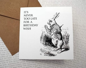 May include: A black and white illustration of the White Rabbit from Alice in Wonderland. The rabbit is holding a pocket watch and has a worried expression on its face. The text "It's never too late for a birthday wish" is printed above the illustration.