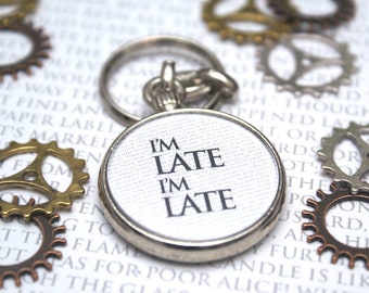 May include: A silver key chain with a round white tag that says "I'm Late I'm Late". The keychain is surrounded by various small metal gears.