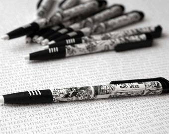 May include: A black and white pen with a design featuring a scene from Alice in Wonderland. The pen has the text "We're all mad here" and a website address.