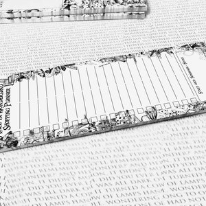 Op de afbeelding: Een zwart-witte Alice in Wonderland-thema boodschappenlijstje notitieboekje. Het notitieboekje heeft een geruite rand en bevat illustraties van personages en objecten uit het boek. De tekst "Alice in Wonderland Shopping Planner" is op het notitieboekje gedrukt.