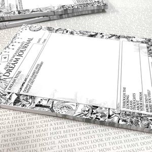 Op de afbeelding: Zwart-wit "Alice in Wonderland" droomdagboek. Het dagboek bevat illustraties en tekst uit het verhaal, met ruimte om dromen op te schrijven. De voorkant leest "Dream Journal" en bevat vragen.