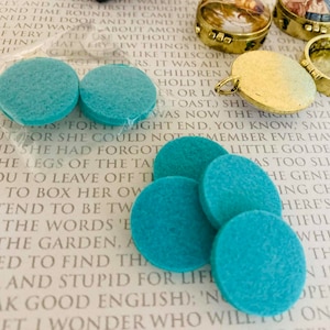 May include: A close-up of seven teal felt circles, approximately 2.5 cm in diameter, arranged in a semi-circle on a white surface with text in the background.