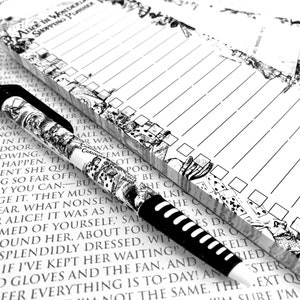 Op de afbeelding: Een zwart-witte pen met een fantasierijk ontwerp met een konijn en speelkaarten. De pen ligt op een wit notitieblok met een zwart-wit Alice in Wonderland-thema. Het notitieblok heeft een geruit gedeelte om op te schrijven en een checklistgedeelte met vakjes.