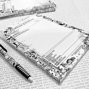 Op de afbeelding: Zwart-wit Alice in Wonderland thema droomdagboek en pen set. Het dagboek heeft een decoratieve rand met illustraties en tekst. De pen heeft een zwart-wit gestreept ontwerp.