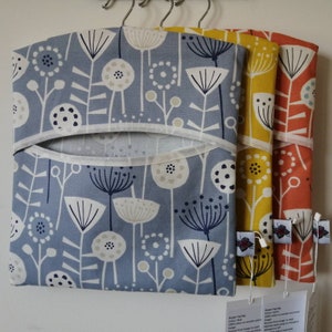 May include: Three hanging storage bags with a floral pattern. The bags are blue, yellow, and orange. The bags are made of fabric and have a white trim. The bags are hanging on a white wall.