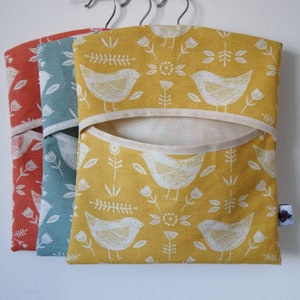 May include: Three hanging fabric storage bags with a white bird and floral pattern. The bags are in orange, teal, and yellow.