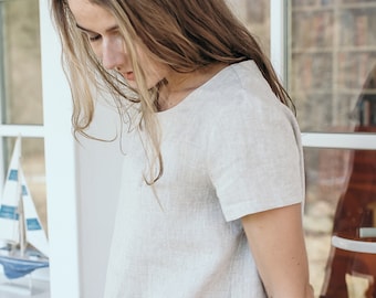 May include: A woman wearing a light gray linen top with short sleeves. The top has a round neckline and a relaxed fit.