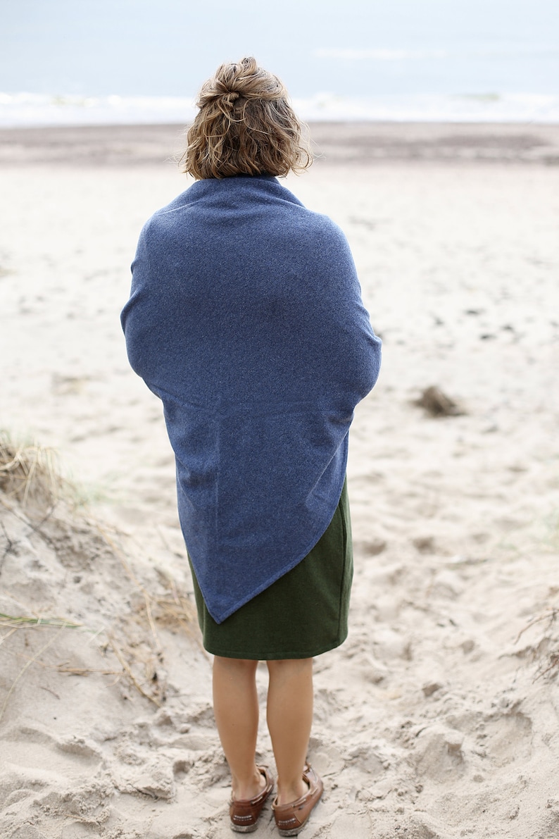 Może przedstawiać: Osoba w niebieskim dzianym szaliku i zielonej sp&oacute;dnicy stojąca na piaszczystej plaży.