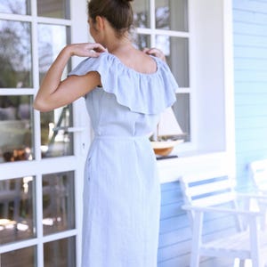 Puede incluir: Un vestido de lino azul claro con un escote de volantes y mangas cortas. El vestido est&aacute; ajustado en el corpi&ntilde;o y se ensancha ligeramente en la falda.