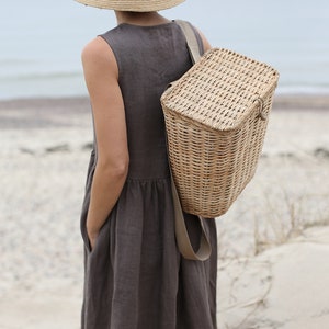 May include: A woman wearing a brown linen dress and a wide-brimmed straw hat carries a woven wicker backpack.