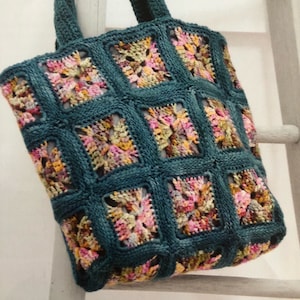 Puede incluir: Una bolsa de mano de crochet de color turquesa con un estampado floral colorido. La bolsa tiene dos asas y está hecha de un hilo suave y texturizado.