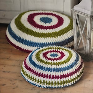 Peut inclure: Deux coussins de sol ronds et crochetés. Le plus grand coussin présente un motif rayé blanc, vert, bleu et bordeaux. Le plus petit coussin a un motif similaire. Les coussins sont sur un sol en bois.