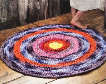 May include: A colorful round crocheted rug with concentric circles of purple, orange, pink, and yellow yarn. The rug is on a wooden floor.