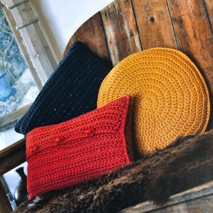 May include: Three crocheted cushions in different colours and textures. A red cushion with buttons, a dark blue cushion, and a round yellow cushion.