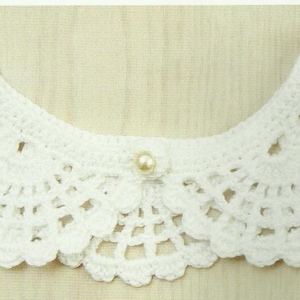 May include: White crocheted collar with a pearl button in the center.