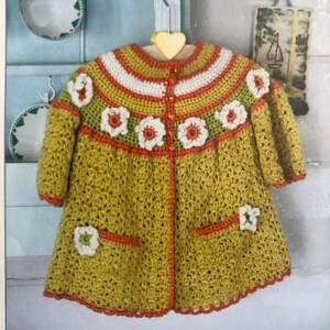 May include: A crocheted cardigan in shades of green, orange, and white with a flower design. The cardigan has pockets and a button closure.