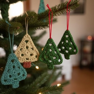 May include: Crocheted Christmas tree ornaments in shades of green and tan hang from a Christmas tree branch. The ornaments are triangular with openwork designs and are suspended by red, blue, and tan strings. The ornaments add a festive touch.