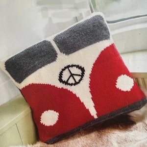 Pode incluir: Uma almofada quadrada de malha com um design vermelho, branco e cinza de uma carrinha de campismo vintage. A almofada tem um símbolo de paz preto e dois círculos brancos. A almofada está sobre uma superfície de pele falsa.