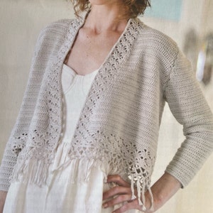 May include: A crocheted cardigan with a delicate lace trim and fringe detail. The cardigan is a light beige color and has a V-neck.