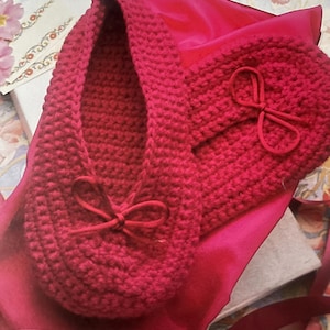 May include: A pair of red crocheted slippers with bows. The slippers are in a gift box with a red satin lining.