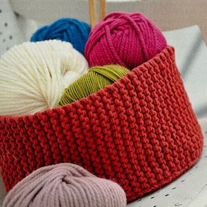 May include: A red knitted basket filled with colorful yarn balls. The yarn is in shades of white, blue, pink, green, and light pink.