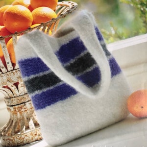May include: A white knitted tote bag with purple, gray, and white stripes. The bag is sitting on a table next to a bowl of oranges.