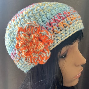 May include: A crocheted hat in shades of blue, yellow, and orange with a large orange crocheted flower on the side.