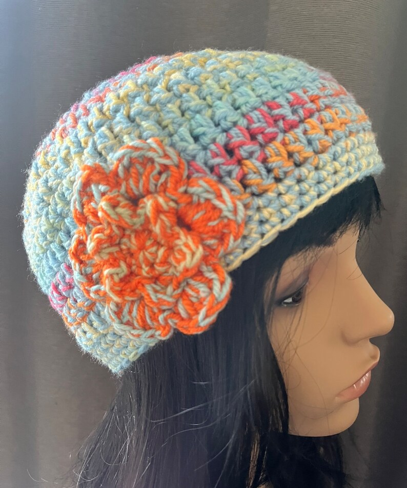 May include: A crocheted hat in shades of blue, yellow, and orange with a large orange crocheted flower on the side.