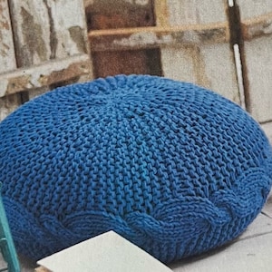 Könnte beinhalten: Ein großer, runder, blauer Strickhocker oder Ottoman. Der Hocker ist aus dickem, grobem Garn gefertigt und hat ein Zopfmuster.
