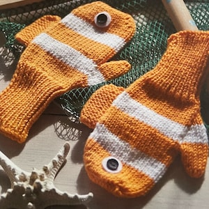 May include: A pair of orange and white striped knitted fingerless gloves shaped like clownfish. Each glove has a black button for an eye.