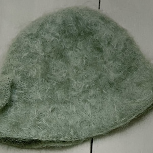 May include: A soft, light green fuzzy hat with a bow on the side.