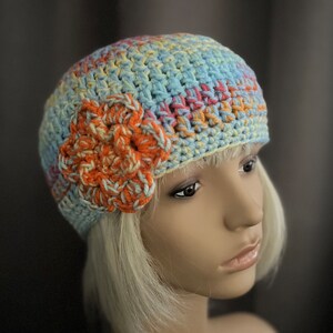 May include: A crocheted hat with a flower design in shades of blue, orange, and yellow. The hat is made with a soft, textured yarn and has a slouchy fit.