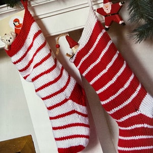 Peut inclure: Deux chaussettes de Noël rayées rouge et blanc accrochées à une cheminée blanche. Les chaussettes sont remplies de petits jouets.