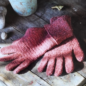 Op de afbeelding: Een paar gehaakte handschoenen in een verloop van roze en rood. De handschoenen zijn gemaakt met een textuur-steek en hebben een pluche uitstraling.