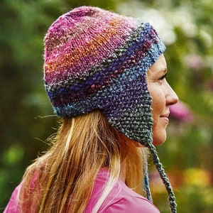 May include: A colorful knitted hat with ear flaps. The hat is made with a variety of shades of blue, purple, pink, and orange yarn. The hat has a long tassel that hangs down the back.