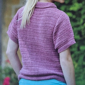 Puede incluir: Una camisa de punto de crochet de color rosa con mangas cortas y cuello.