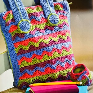 May include: A colorful crocheted tote bag with green, purple, blue, and pink stripes. The bag has two blue handles and two green crocheted buttons.