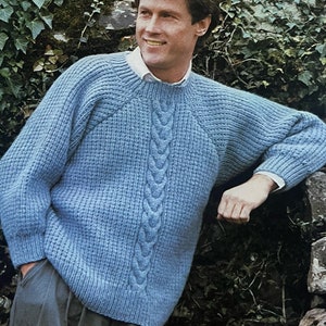 Può includere: Un maglione blu a maglia con un motivo a treccia sul davanti. Il maglione ha un collo rotondo e maniche lunghe.