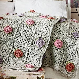 May include: A crocheted throw blanket with a granny square pattern and floral accents in shades of pink, purple, and green.