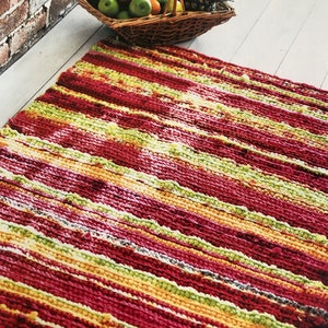 May include: A colorful striped rug with red, yellow, green, and white stripes. The rug is made of a thick, textured yarn and has a slightly distressed look.