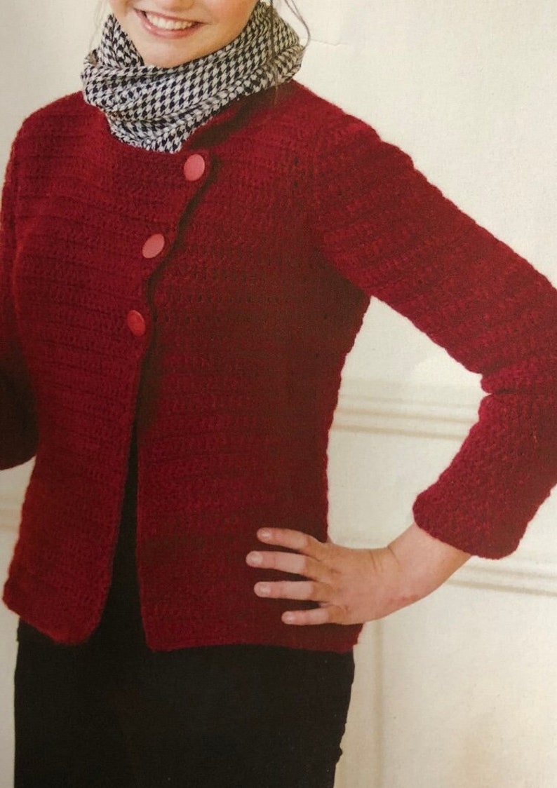May include: A red crocheted cardigan with three pink buttons. The cardigan has a slightly asymmetrical closure and long sleeves.