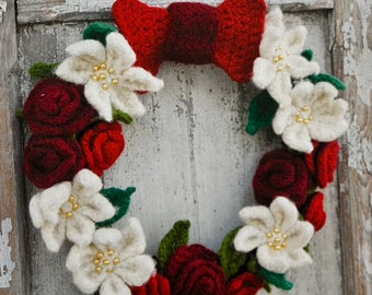 May include: A red and white crocheted wreath with a red bow in the center. The wreath is made of white flowers and red roses.