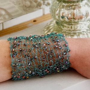 May include: A teal blue wire bracelet with iridescent beads woven into the design.