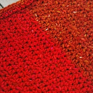 May include: A close-up of a red crocheted fabric with a diagonal line of a darker red and orange crocheted fabric.