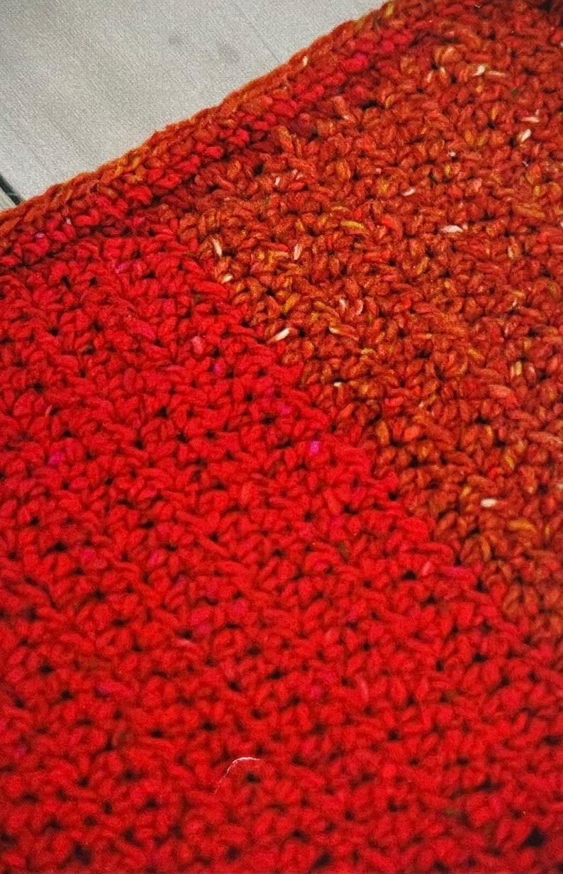 May include: A close-up of a red crocheted fabric with a diagonal line of a darker red and orange crocheted fabric.